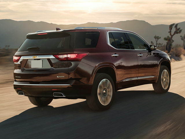 Profile view of a burgundy 2021 Chevrolet Traverse being driven on the road with mountains far off in the background. | Collision Center | Crain Automotive Team Collision
